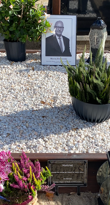 The memorial plaque made for Jan Elzinga at the grave in Kozmin, Poland, among flowers and planting.